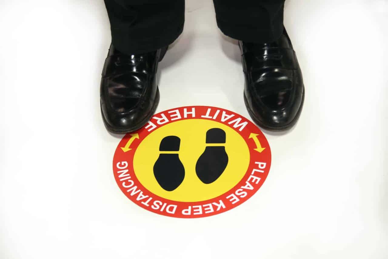 Man in dress shoes standing at a social distancing graphic