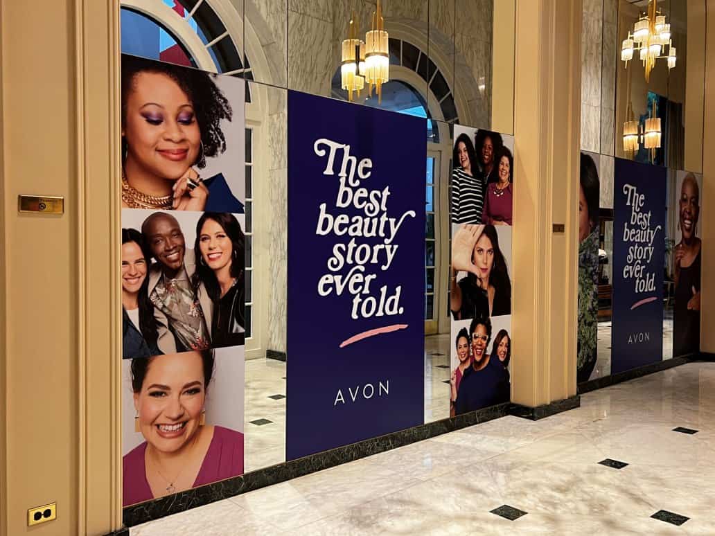 A wall with visuals for events for a beauty brand featuring the company name and several customers faces A wall with visuals for events for a beauty brand featuring the company name and several customers faces
