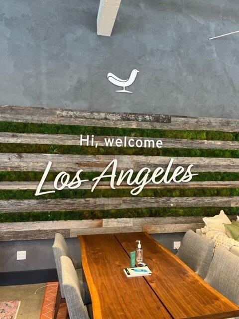 welcome LA2 a wooden table sitting under a welcome sign.