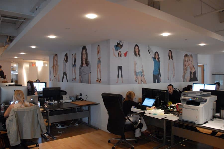 modern open office space,  workers sitting in chairs in front of  desks and a custom wall wrap featuring several women wearing different types of clothes modern open office space, workers sitting in chairs in front of desks and a custom wall wrap featuring several women wearing different types of clothes