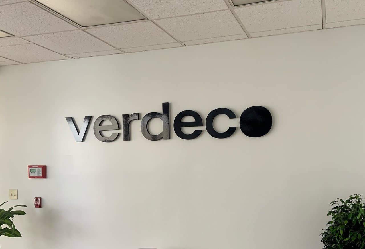 Verdeco croped a white wall with a sign that says verddeco on it.
