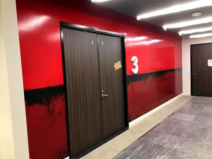red wall a hallway with three doors and a number on the wall.