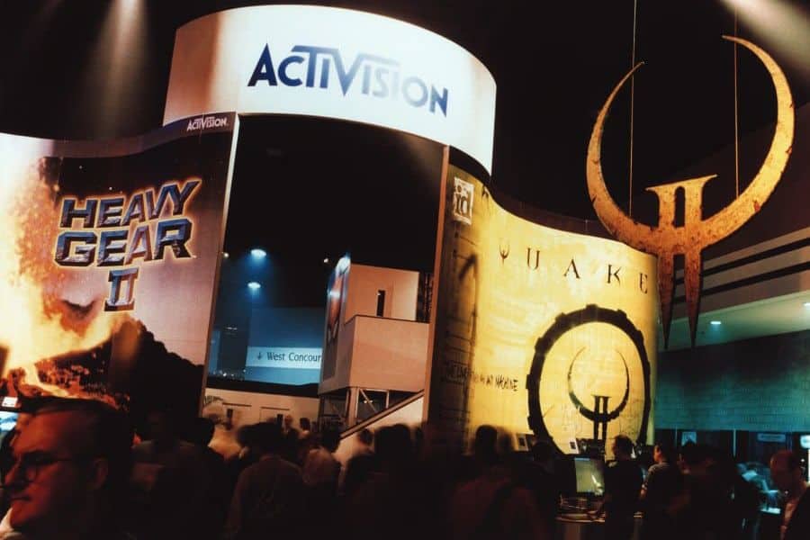 Photo of a bustling trade show booth with signs for "activision," "heavy gear ii," and "quake." a large, illuminated ring hangs above the crowd, casting a warm glow on the busy exhibit area. Photo of a bustling trade show booth with signs for "activision," "heavy gear ii," and "quake." a large, illuminated ring hangs above the crowd, casting a warm glow on the busy exhibit area.