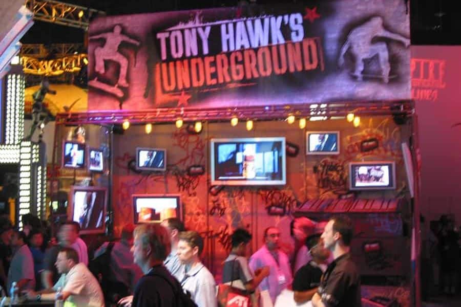 Crowded exhibition booth for "tony hawk's underground" at a gaming event. the booth has vibrant graffiti decor and multiple screens displaying the game, with attendees watching and interacting. Crowded exhibition booth for "tony hawk's underground" at a gaming event. the booth has vibrant graffiti decor and multiple screens displaying the game, with attendees watching and interacting.