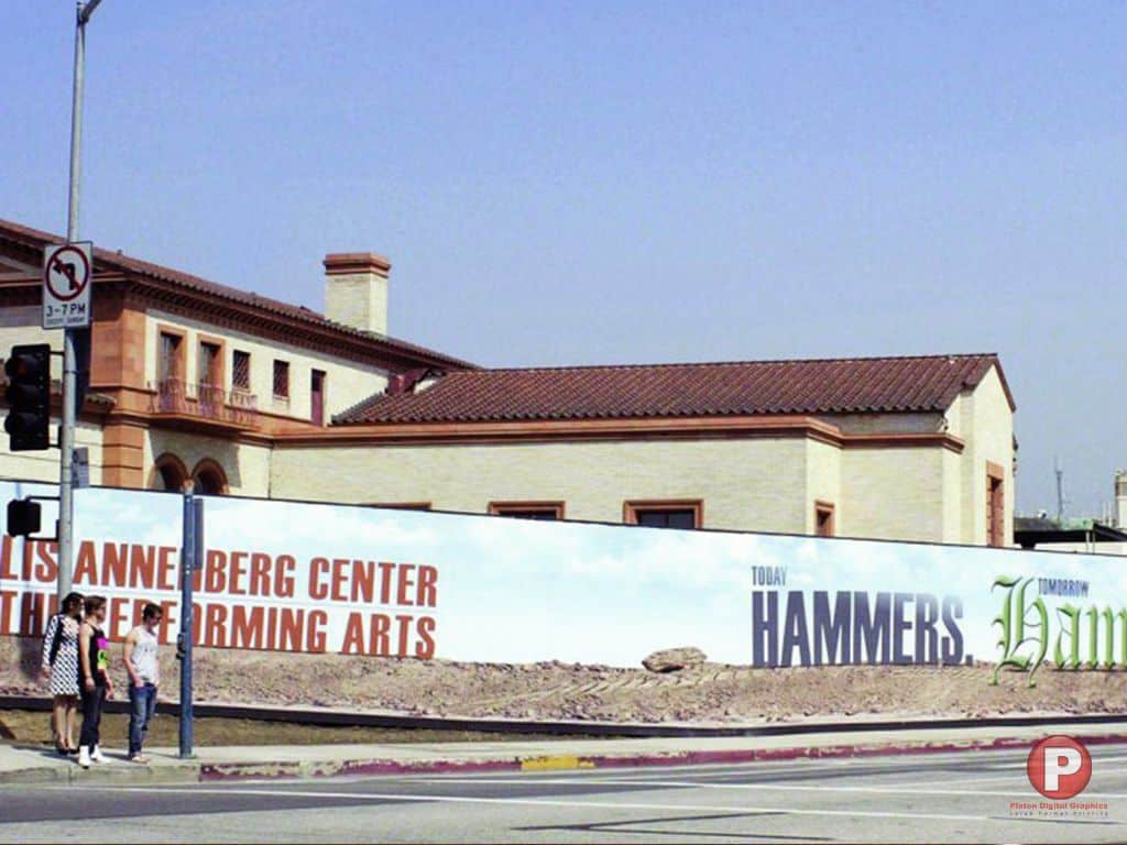 Three people stand on a sidewalk near a street corner, next to a large construction site banner that reads, 